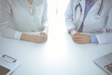 Doktor ve hasta klinikteki masada yan yana oturuyorlar, yakın plan. Tıp konsepti.