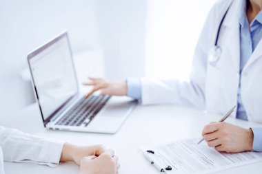 Doktor ve hasta bir şey tartışıyor ve klinikteki masada karşılıklı otururken dizüstü bilgisayar kullanıyorlar. Mükemmel tıbbi hizmet ve tıp konsepti.