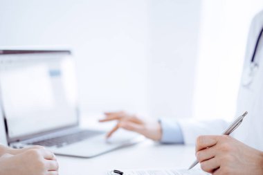 Doktor ve hasta bir şey tartışıyor ve klinikteki masada karşılıklı otururken dizüstü bilgisayar kullanıyorlar. Mükemmel tıbbi hizmet ve tıp konsepti.