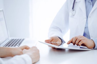 Doktor ve hasta klinikteki masada karşılıklı oturuyorlar. Tablet bilgisayar kullanan kadın doktorların ellerine odaklan, kapat. Tıp konsepti.