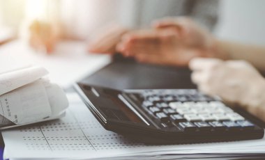 Müşteri ile vergi sayarken ve tartışırken kalem ve dizüstü bilgisayar kullanan kadın muhasebeci, hesap makinesine odaklan. İş denetimi ve finans kavramları.