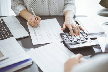 Müşteri ya da meslektaşıyla birlikte vergi sayarken hesap makinesi ve dizüstü bilgisayar kullanan kadın muhasebeci. İş denetleme ekibi, finans danışmanı.