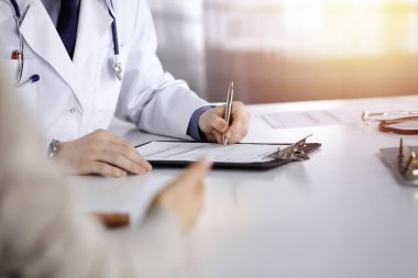 Bilinmeyen bir erkek doktor ve hasta kadın karanlık bir klinikte otururken bir şey tartışıyorlar ve arka planda pano kullanıyorlar..