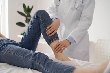 Doktor ve hasta klinikte olağan sağlık kontrolündeler. Terapist genç bir kadının dizini muayene ediyor. Tıp konsepti .