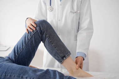 Doktor ve hasta klinikte olağan sağlık kontrolündeler. Terapist genç bir kadının dizini muayene ediyor. Tıp konsepti .