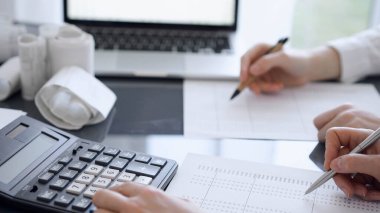 İki muhasebeci vergi veya gelir dengesi saymak için bir hesap makinesi ve dizüstü bilgisayar kullanıyor. İş, denetim ve vergi kavramları.