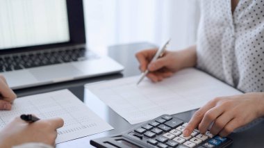 İki muhasebeci vergi veya gelir dengesi saymak için bir hesap makinesi ve dizüstü bilgisayar kullanıyor. İş, denetim ve vergi kavramları.