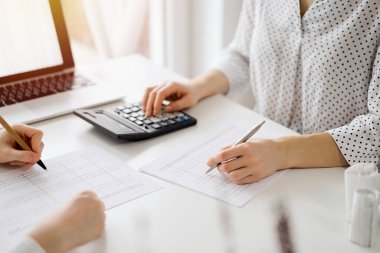 Ofisteki beyaz masada vergileri saymak için hesap makinesi ve dizüstü bilgisayar kullanan iki muhasebeci. İş denetimi ve finans alanında takım çalışması.