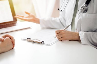Doktor ve hasta klinikteki beyaz masada oturup bir şeyler tartışıyorlar. Kadın doktor dizüstü bilgisayarın ekranına işaret ediyor. Tıp konsepti.