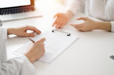 Doktor ve hasta klinikteki beyaz masada yan yana oturuyorlar. Kadın hekim bir kayıt formunu doldururken dinliyor. Tıp konsepti.