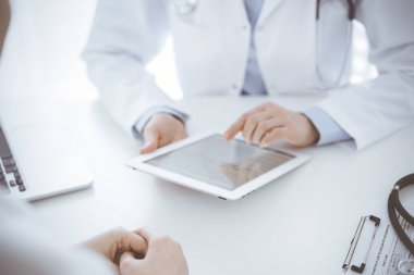 Doktor ve hasta klinikteki masada karşılıklı oturuyorlar. Tablet bilgisayar kullanan kadın doktorların ellerine odaklan, kapat. Tıp konsepti.
