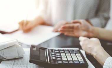 Müşteri ile vergi sayarken ve tartışırken kalem ve dizüstü bilgisayar kullanan kadın muhasebeci, hesap makinesine odaklan. İş denetimi ve finans kavramları.