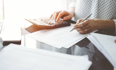 Müşteri için vergi sayarken hesap makinesi ve dizüstü bilgisayar kullanan kadın muhasebeci. İş denetimi ve finans kavramları.