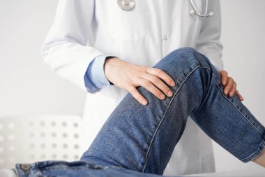 Doktor ve hasta klinikte olağan sağlık kontrolündeler. Terapist genç bir kadının dizini muayene ediyor. Tıp konsepti .