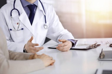 Bilinmeyen bir erkek doktor ve hasta kadın karanlık bir klinikte otururken bir şey tartışıyorlar, arka planda ışık parlıyor. Ellerin yakın çekimi.
