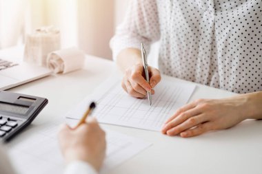 Ofisteki beyaz masada vergileri saymak için dizüstü bilgisayar ve hesap makinesi kullanan iki muhasebeci. İş denetimi ve finans alanında takım çalışması.