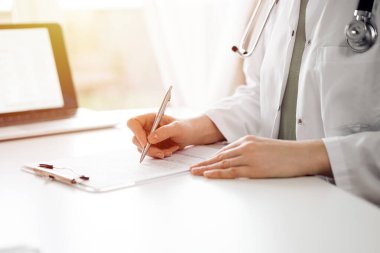 Doktor ve hasta klinikteki beyaz masada yan yana oturuyorlar. Kadın hekim bir kayıt formunu doldururken dinliyor. Tıp konsepti.
