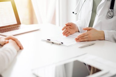 Doktor ve hasta klinikteki beyaz masada oturup bir şeyler tartışıyorlar. Kadın hekim bir kayıt formunu doldururken dinliyor. Tıp konsepti.