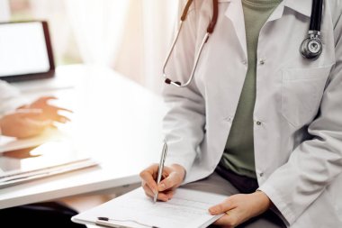 Doktor ve hasta görüşü. Kadın hekim, tıbbi muayene olan bir kadının karşısındaki kayıtları dolduruyor. Tıp konsepti.