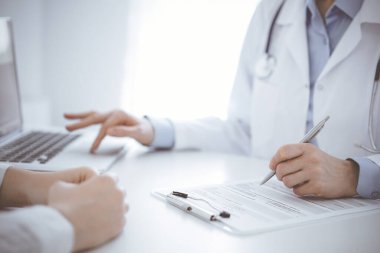 Doktor ve hasta bir şey tartışıyor ve klinikteki masada karşılıklı otururken dizüstü bilgisayar kullanıyorlar. Mükemmel tıbbi hizmet ve tıp konsepti.