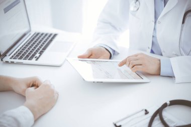 Doktor ve hasta klinikteki masada karşılıklı oturuyorlar. Tablet bilgisayar kullanan kadın doktorların ellerine odaklan, kapat. Tıp konsepti.