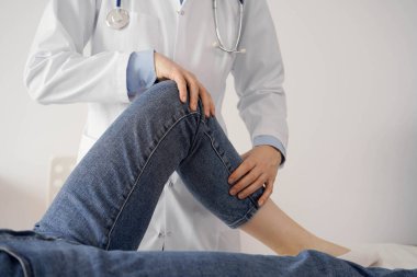 Doktor ve hasta klinikte olağan sağlık kontrolündeler. Terapist genç bir kadının dizini muayene ediyor. Tıp konsepti .