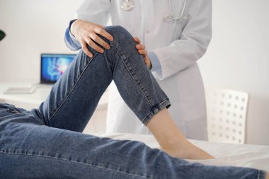 Doktor ve hasta klinikte olağan sağlık kontrolündeler. Terapist genç bir kadının dizini muayene ediyor. Tıp konsepti .