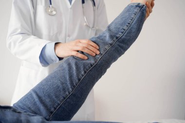 Doktor ve hasta klinikte olağan sağlık kontrolündeler. Terapist genç bir kadının dizini muayene ediyor. Tıp konsepti .