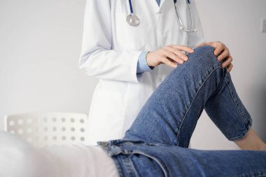 Doktor ve hasta klinikte olağan sağlık kontrolündeler. Terapist genç bir kadının dizini muayene ediyor. Tıp konsepti .