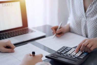 İki muhasebeci vergi veya gelir dengesi saymak için bir hesap makinesi ve dizüstü bilgisayar kullanıyor. İş, denetim ve vergi kavramları.