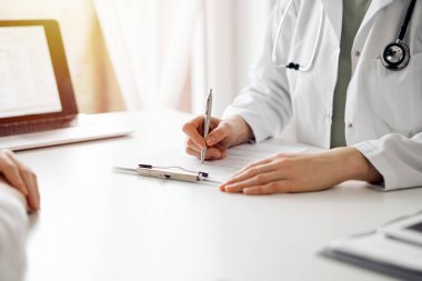 Doktor ve hasta klinikteki beyaz masada yan yana oturuyorlar. Kadın hekim bir kayıt formunu doldururken dinliyor. Tıp konsepti.