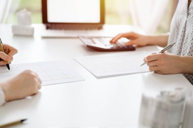 Hesap makinesi ve dizüstü bilgisayar kullanan iki muhasebeci vergileri ve gelir dengesini hesaplamak için beklerken makbuzlar da hesaplanmayı bekliyor. İş denetimi ve vergi kavramları.