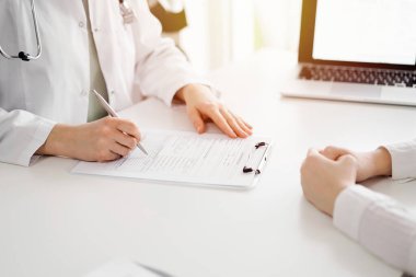 Doktor ve hasta klinikteki beyaz masada yan yana oturuyorlar. Kadın hekim bir kayıt formunu doldururken dinliyor. Tıp konsepti.