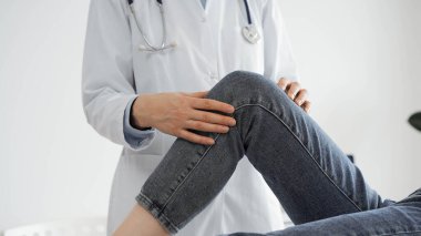 Doktor ve hasta klinikte olağan sağlık kontrolündeler. Terapist genç bir kadının dizini muayene ediyor. Tıp konsepti .