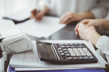 Müşteri ile vergi sayarken ve tartışırken kalem ve dizüstü bilgisayar kullanan kadın muhasebeci, hesap makinesine odaklan. İş denetimi ve finans kavramları.