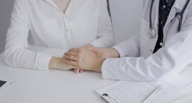 Doktor ve bir hasta. Koyu mavi noktalı bluzun üzerine beyaz bir ceket giyen kadın doktor klinikteki muayene sırasında bir kadına güven veriyor. Tıp konsepti.