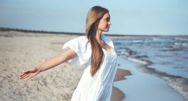 Mutlu gülümseyen güzel kadın okyanus sahilinde beyaz bir yaz elbisesi içinde, kolları açık..