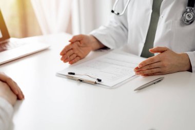 Doktor ve hasta klinikteki beyaz masada oturup bir şeyler tartışıyorlar. Kadın hekim bir kayıt formunu doldururken dinliyor. Tıp konsepti.