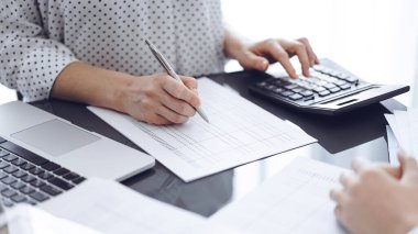 Müşteri için vergi sayarken hesap makinesi ve dizüstü bilgisayar kullanan kadın muhasebeci. İş denetimi kavramları.