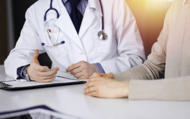 Bilinmeyen bir erkek doktor ve hasta kadın karanlık bir klinikte otururken bir şey tartışıyorlar, arka planda ışık parlıyor. Ellerin yakın çekimi.