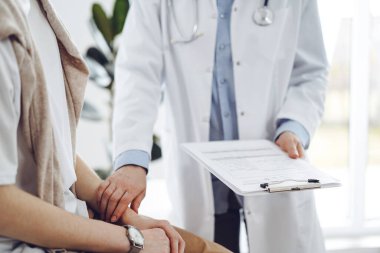 Doktor ve hasta klinikte. Bir yandan dostane bir doktor genç bir kadını muayene ederken diğer yandan tıbbi kayıtlarla dolu bir pano tutuyor. Tıp konsepti.