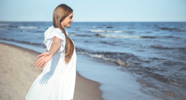 Okyanus sahilinde beyaz bir yaz elbisesi içinde kollarını açmış mutlu, güzel bir kadın..