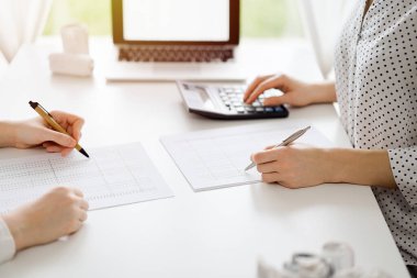 Hesap makinesi ve dizüstü bilgisayar kullanan iki muhasebeci vergileri ve gelir dengesini hesaplamak için beklerken makbuzlar da hesaplanmayı bekliyor. İş denetimi ve vergi kavramları.