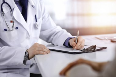 Unknown male doctor and patient woman discussing something while sittingin a darkened clinic and using clipboard, glare of light on the background. clipart