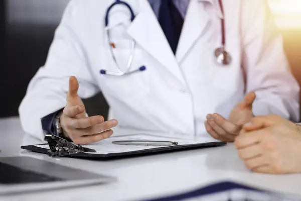 stock image Unknown male doctor and patient woman discussing something while sittingin a darkened clinic, glare of light on the background. Close-up of hands.