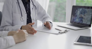 Doktor ve bir hasta dizüstü bilgisayarın yanındaki masada bir şey tartışıyorlar. Tanımlanamayan insanların ellerini kapatıyorlar. Tıp konsepti.
