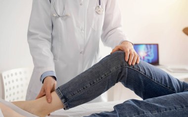 Doktor ve hasta klinikteki sağlık kontrolündeler. Ortopedik genç bir kadının dizini muayene eder. Tıp konsepti.