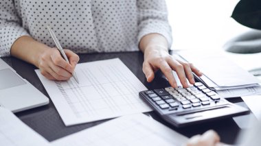 Müşteri ya da meslektaşıyla birlikte vergi sayarken hesap makinesi ve dizüstü bilgisayar kullanan kadın muhasebeci. İş denetleme ekibi, finans danışmanı.