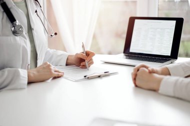 Doktor ve hasta klinikteki beyaz masada yan yana oturuyorlar. Kadın hekim bir kayıt formunu doldururken dinliyor. Tıp konsepti.