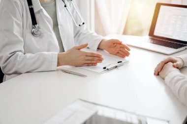 Doktor ve hasta klinikteki beyaz masada oturup bir şeyler tartışıyorlar. Kadın hekim bir kayıt formunu doldururken dinliyor. Tıp konsepti.